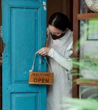 woman in face mask putting out open sign on front door